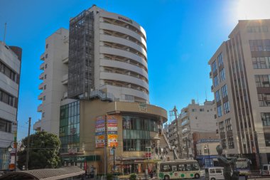 Modern mimariyle çevrili, berrak mavi gökyüzünün altında yürüyen insanların siluetleri. 4 Aralık 2024