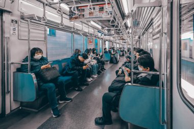 9 Aralık 2024 Bir metro treninde oturan, bazıları mobil cihazlar kullanan,