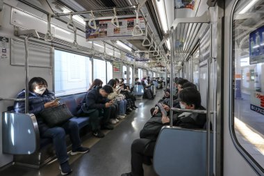 9 Aralık 2024 Bir metro treninde oturan, bazıları mobil cihazlar kullanan,