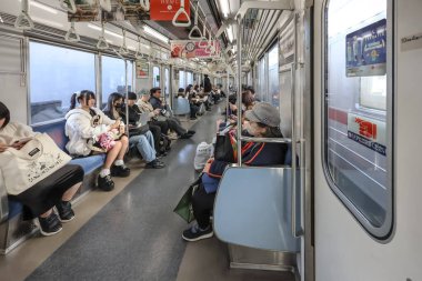 9 Aralık 2024 Bir metro treninde oturan, bazıları mobil cihazlar kullanan,