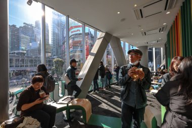 9 Aralık 2024 'te müşterilerin yemek yediği kafe sahnesi, hareketli bir şehir arkaplanı görüntüsü.