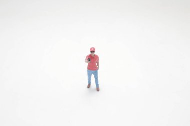 Sıradan giyinmiş, elinde akıllı telefon tutan minyatür bir figür.