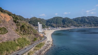 23 Mart 2025 Bir kıyı şeridi manzaralı bir yol, binalar ve görkemli yeşil