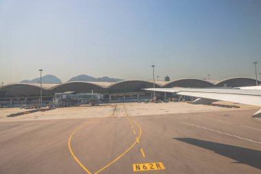 22 Mart 2025 uçak penceresi bir kanat, pist ve modern havaalanı terminalini gösteriyor.