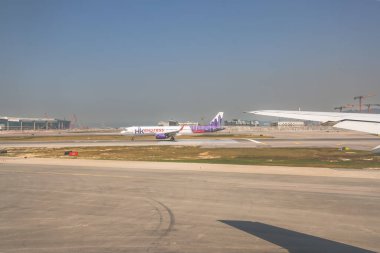 22 Mart 2025 uçak penceresi bir kanat, pist ve modern havaalanı terminalini gösteriyor.