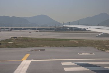 22 Mart 2025 uçak penceresi bir kanat, pist ve modern havaalanı terminalini gösteriyor.