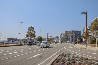 23 Mart 2025 Araçlar, palmiye ağaçları ve çağdaş binalar ile hareketli bir şehir caddesi