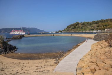 Feribot, mavi gökyüzü ve ahşap kaplamalı sakin bir sahil manzarası.