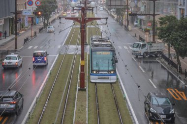 Çağdaş bir tramvay yağmurlu şehirlerde yeşil yollar boyunca seyahat ediyor.,