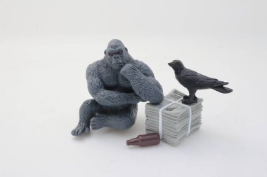 Bir goril, karga ve bir yığın gazetenin yer aldığı tuhaf bir oyuncak düzenlemesi.,