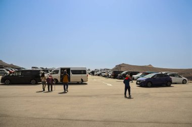 Açık mavi gökyüzünün altındaki kayalık dağların yakınındaki otoparkta.