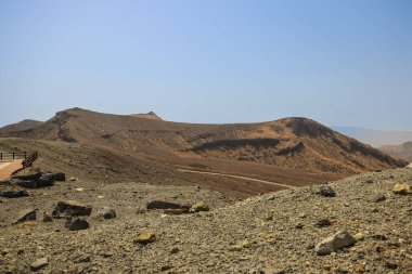Uzak küçük kulübelerin olduğu çorak çöl manzarası, açık mavi bir gökyüzü.