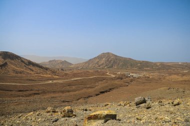 Uzak küçük kulübelerin olduğu çorak çöl manzarası, açık mavi bir gökyüzü.