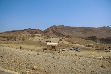 Uzak küçük kulübelerin olduğu çorak çöl manzarası, açık mavi bir gökyüzü.