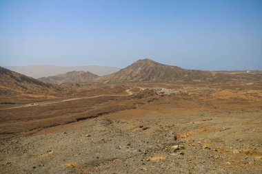 Uzak küçük kulübelerin olduğu çorak çöl manzarası, açık mavi bir gökyüzü.