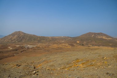 Uzak küçük kulübelerin olduğu çorak çöl manzarası, açık mavi bir gökyüzü.