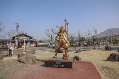 Yakındaki ağaçların olduğu bir parkta sergilenen altın heykel