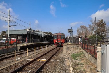 Güneşli bir günde kalabalık bir tren istasyonuna bir tren gelir.,