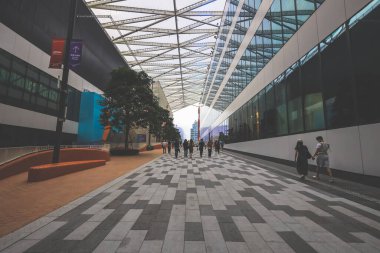 Geniş bir yaya yolu modern cam binalar ve ağaçlarla kaplı.,