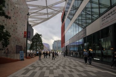 Geniş bir yaya yolu modern cam binalar ve ağaçlarla kaplı.,
