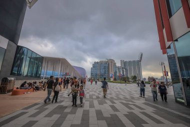 Geniş bir yaya yolu modern cam binalar ve ağaçlarla kaplı.,