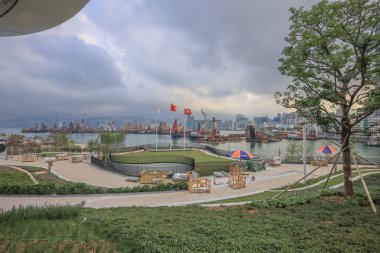 Tekneler, bayraklar ve bulutlu gökyüzünün altında yeşil bir park manzarası olan liman..