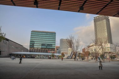 24 Mart 2025 24 Mart 2025 24 Mart 2025 modern bina ve kamu plazası açık gökyüzü altında, kent yaşamı sergilenmektedir