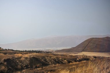 Açık arazilerle çevrili büyük kahverengi bir tepenin huzurlu manzarası.
