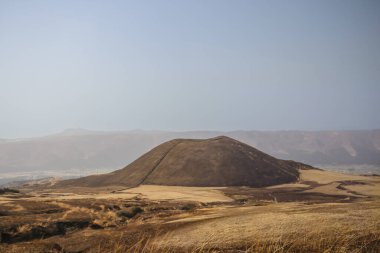 Açık arazilerle çevrili büyük kahverengi bir tepenin huzurlu manzarası.