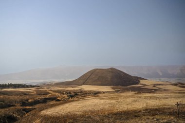 Açık arazilerle çevrili büyük kahverengi bir tepenin huzurlu manzarası.