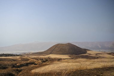 Açık arazilerle çevrili büyük kahverengi bir tepenin huzurlu manzarası.