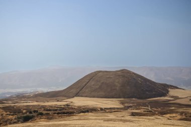 Açık arazilerle çevrili büyük kahverengi bir tepenin huzurlu manzarası.