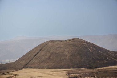 Açık arazilerle çevrili büyük kahverengi bir tepenin huzurlu manzarası.