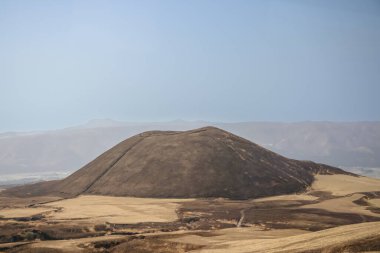 Açık arazilerle çevrili büyük kahverengi bir tepenin huzurlu manzarası.