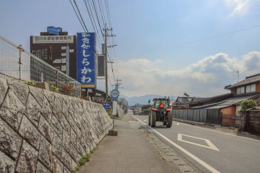 Huzurlu kırsal yol, geleneksel mimarinin yanında parlak bir gökyüzü altında.