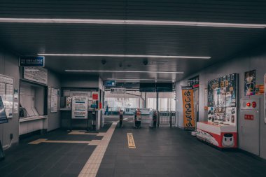 Tren istasyonunun içi oturma yerlerini, bavullu insanları ve tabelaları gösteriyor.