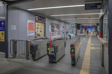 Tren istasyonunun içi oturma yerlerini, bavullu insanları ve tabelaları gösteriyor.