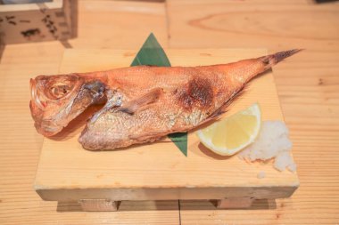 Tahta bir tabakta limon dilimi ve garnitürle sunulmuş ızgara balık.