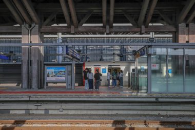 İnsanlar modern mimariyle çevrili bir tren istasyonunda bekliyorlar.