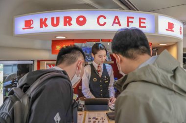 Bir kafe çalışanı şık bir kahve tezgahında müşterilere yardım eder.,