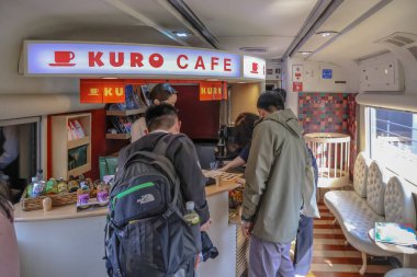 Bir kafe çalışanı şık bir kahve tezgahında müşterilere yardım eder.,
