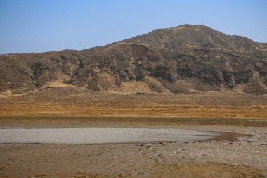 Ön planda küçük bir su birikintisi olan kuru, düz bir arazi.