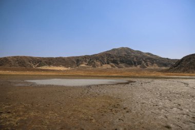 Ön planda küçük bir su birikintisi olan kuru, düz bir arazi.