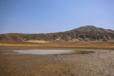 Ön planda küçük bir su birikintisi olan kuru, düz bir arazi.
