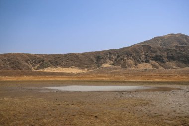 Ön planda küçük bir su birikintisi olan kuru, düz bir arazi.