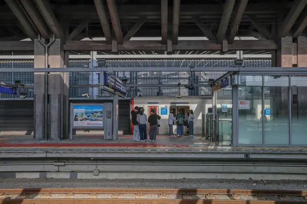 İnsanlar modern mimariyle çevrili bir tren istasyonunda bekliyorlar.