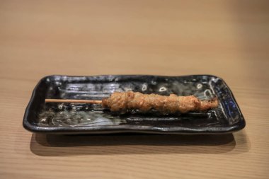 Yakitori şişi seramik siyah bir tabakta sunuluyor.