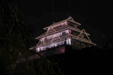 Pembe ışıklar geleneksel bir Japon kalesini aydınlatıyor.,