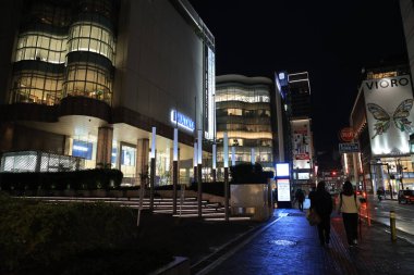 Alışveriş merkezi geceleri aydınlanıyor, insanlar yürüyor ve bisiklete biniyor.