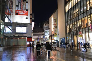 Alışveriş merkezi geceleri aydınlanıyor, insanlar yürüyor ve bisiklete biniyor.